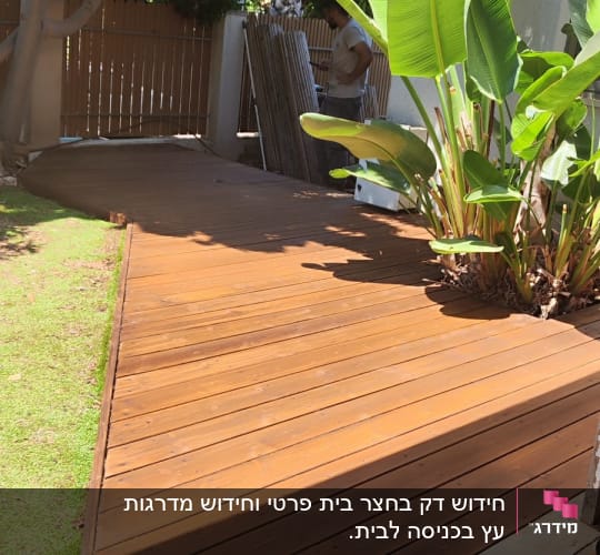 דק עץ בגינה עם צמחייה ועובד ברקע
